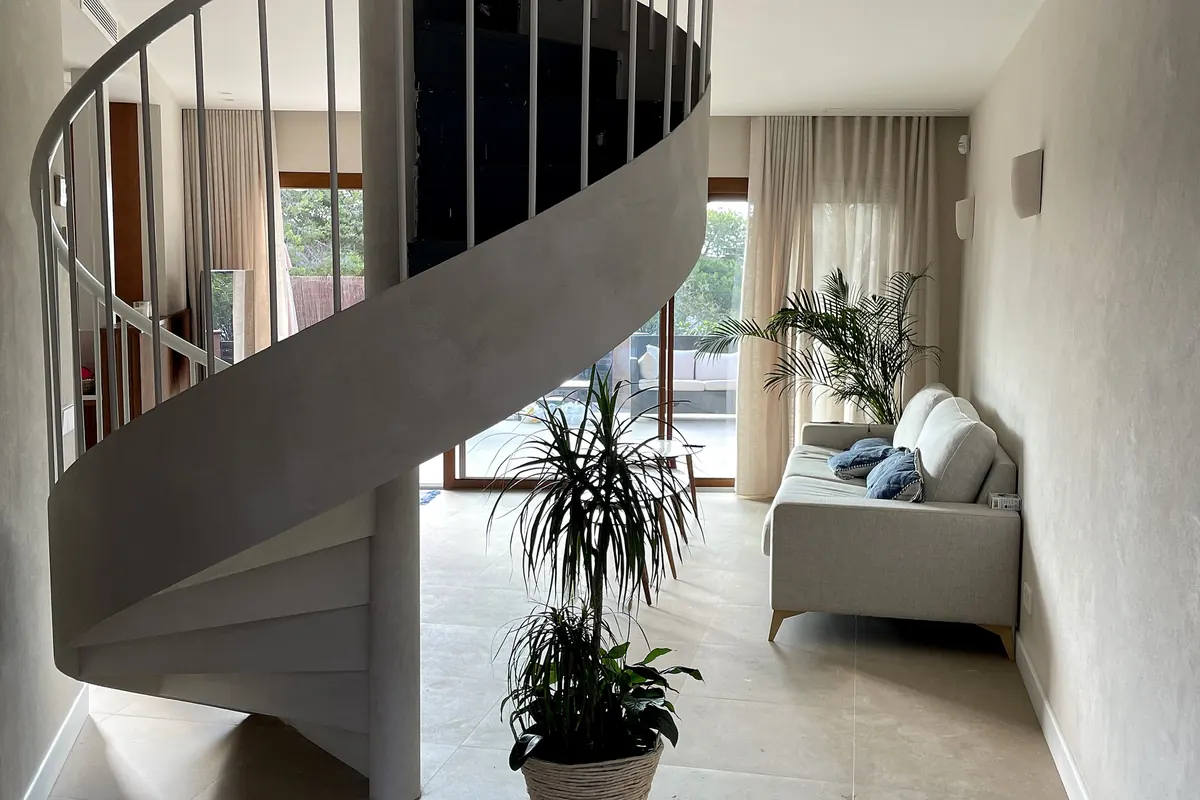 Escalera helicoidal revestida en microcemento MicroStone junto a un salón con luz natural y paredes de cal